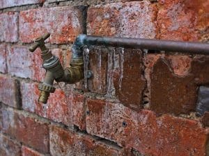 Leaky faucet with icicles attached to an exterior brick wall.