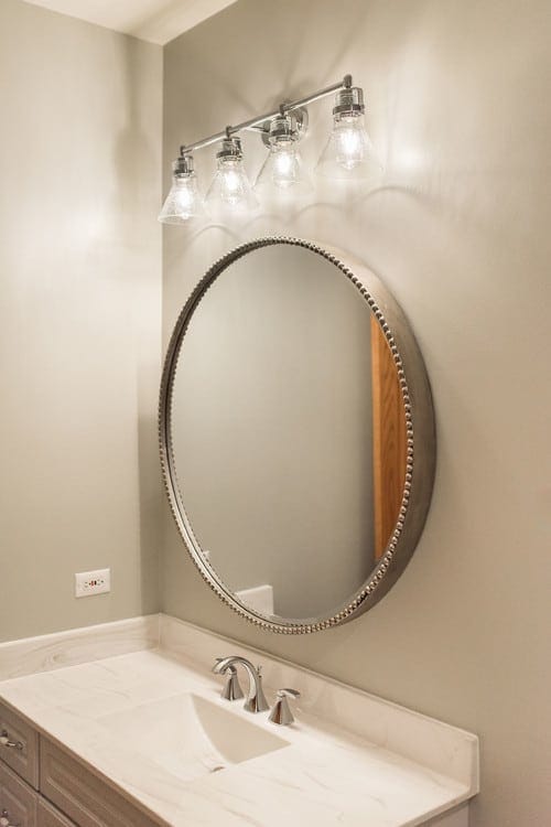 Large oval mirror with a decorative light fixture above it. Bathroom remodel by Spears Design Build Group.
