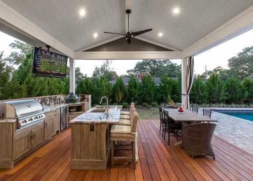 Outdoor deck kitchen and dining area with grill, sink, refrigerator, and counter, situated next to an inground pool for entertaining.