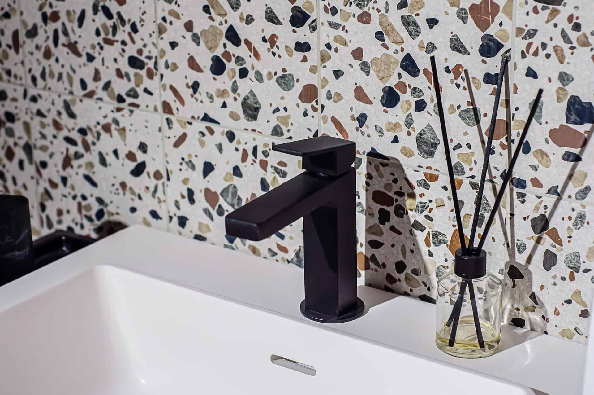 black faucet on the washbasin in the bathroom, the wall is decorated with terrazzo style tiles
