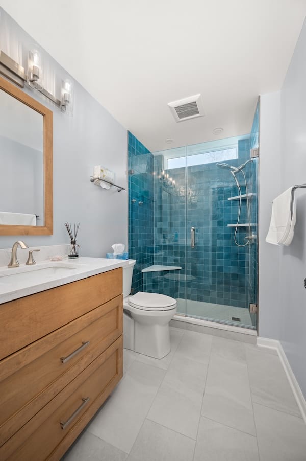 Guest hallway bathroom makeover showing off new vanity, toilet, and shower with new blue tile.