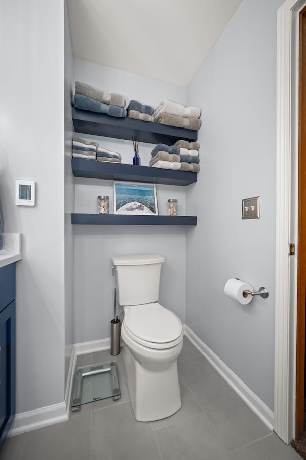 Master bathroom refresh with new toilet and shelving installed above toilet for storage